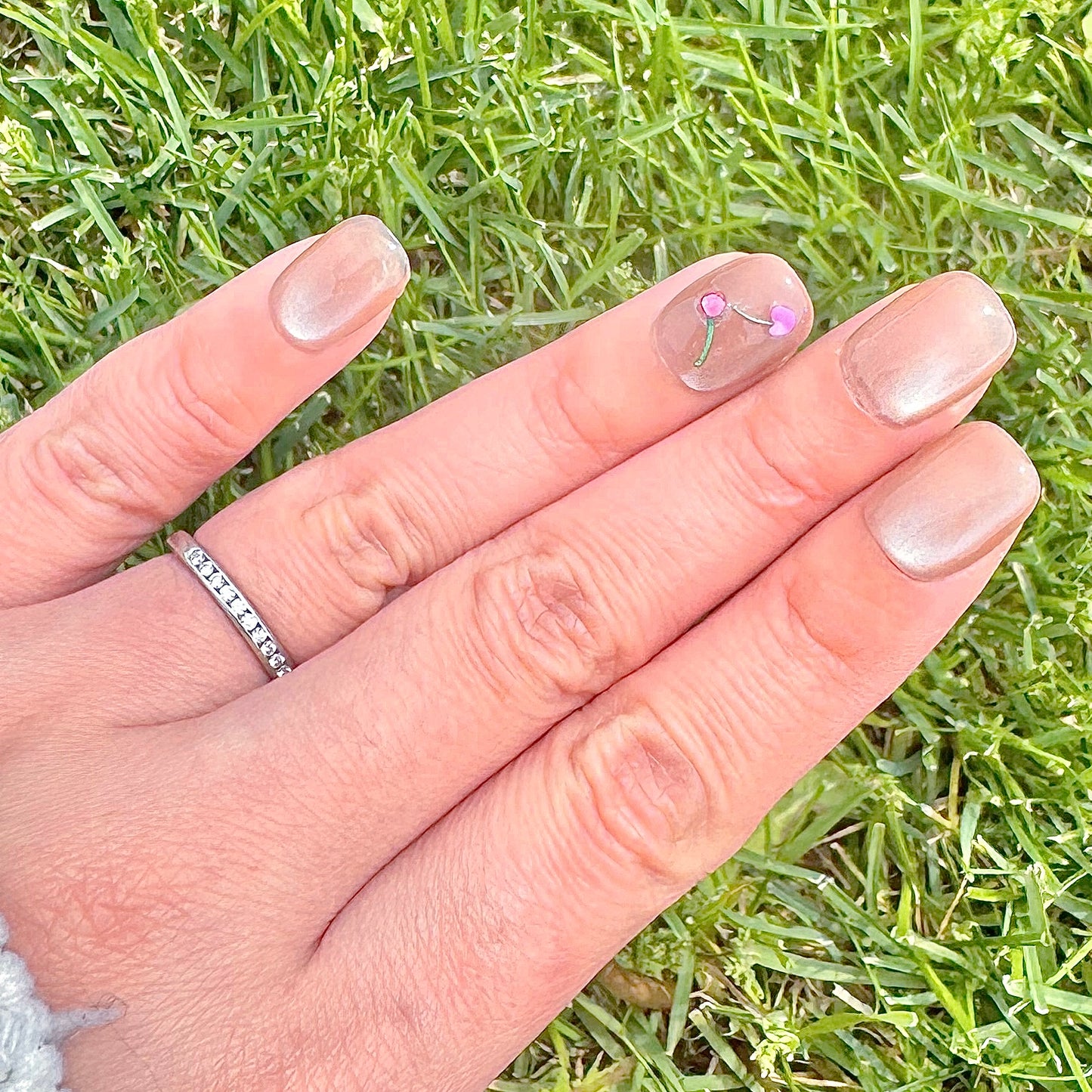 A close-up photo showcases several Cherry Cat Eye press-on nails. The nails boast a captivating, multi-dimensional cat eye finish that appears to shift and shimmer. Dazzling cherry crystals are delicately placed on each nail, adding a touch of sweetness and sophistication.