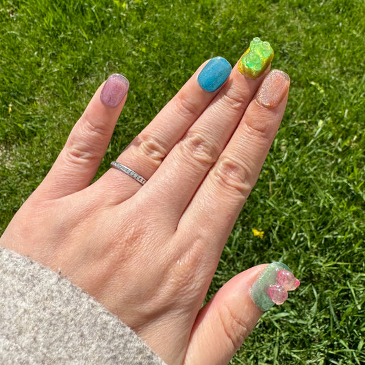 A stunning display of press-on nails styled as gummy bears with a cateye effect. Each nail is designed in vibrant colors representing different flavors: lemon (bright yellow), green apple (vivid green), cherry (rich red), blueberry (soft blue), grape (deep purple), and lime (tangy green). The cateye effect gives each nail a shimmering, multi-dimensional look, capturing the light beautifully. Perfect for a fun and fashionable manicure.