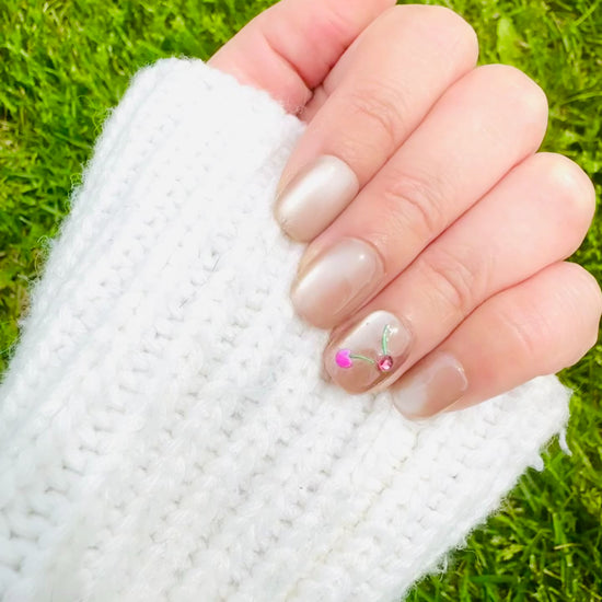 A close-up photo showcases several Cherry Cat Eye press-on nails. The nails boast a captivating, multi-dimensional cat eye finish that appears to shift and shimmer. Dazzling cherry crystals are delicately placed on each nail, adding a touch of sweetness and sophistication.