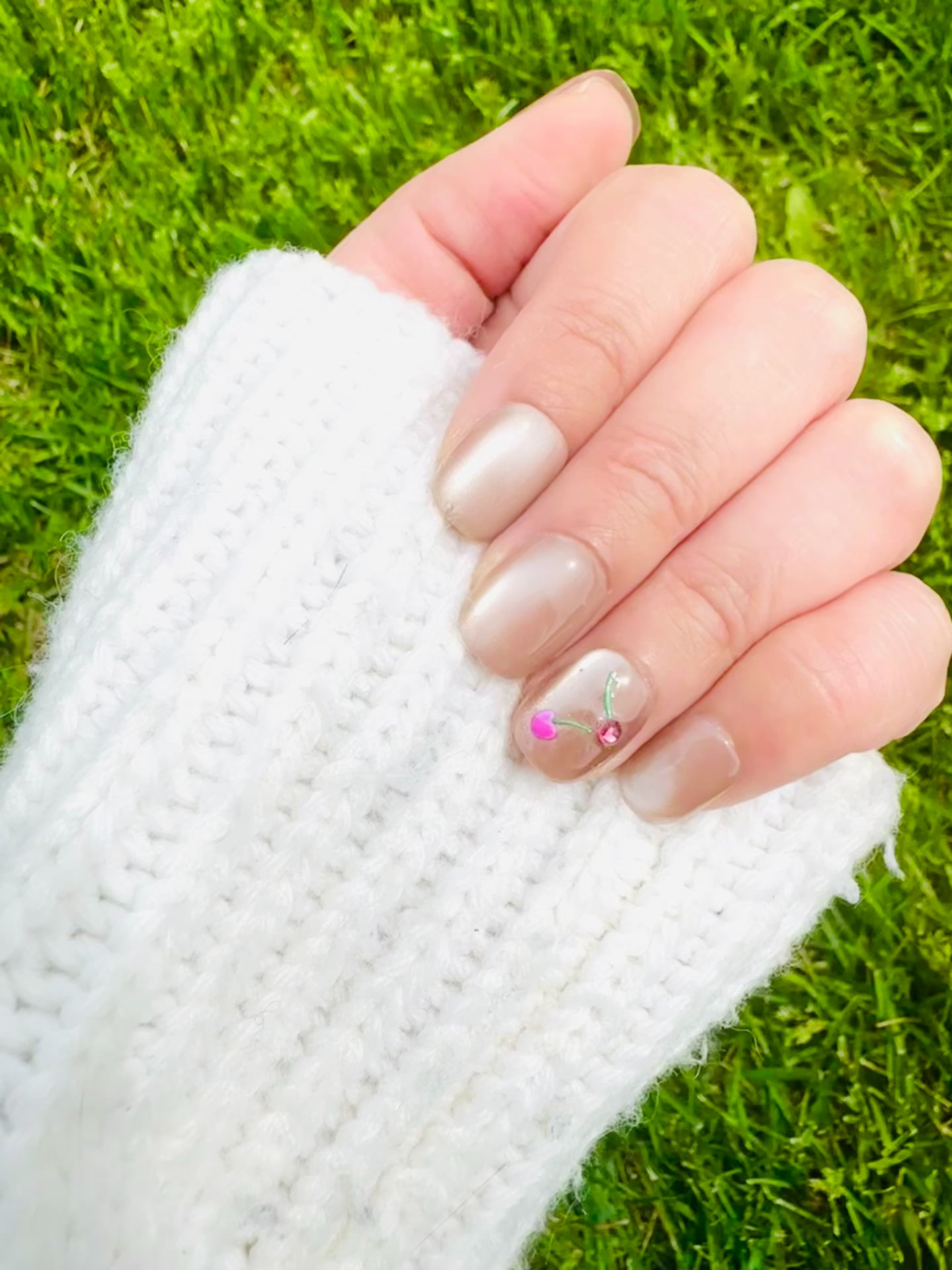 A close-up photo showcases several Cherry Cat Eye press-on nails. The nails boast a captivating, multi-dimensional cat eye finish that appears to shift and shimmer. Dazzling cherry crystals are delicately placed on each nail, adding a touch of sweetness and sophistication.